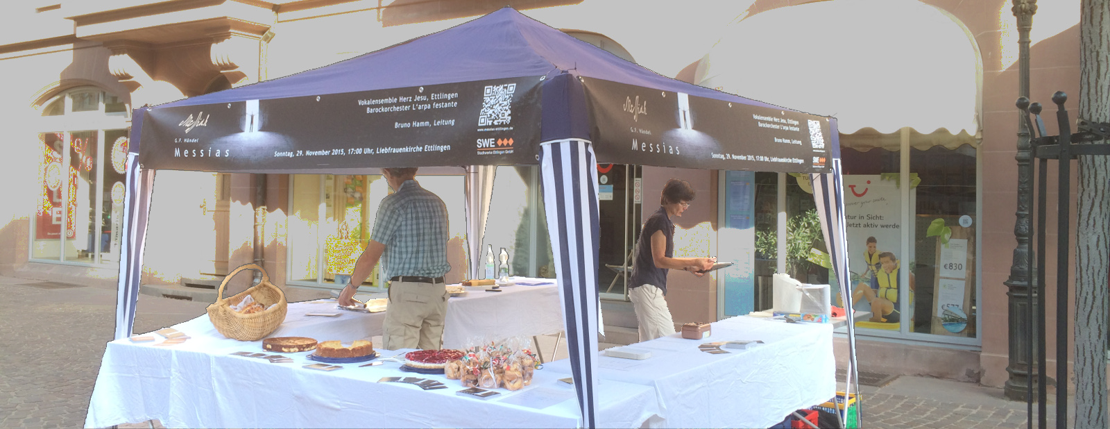 Ein Bild des Kuchverkaufsstands auf dem Wochenmarkt, mit Bannern an drei Seiten.